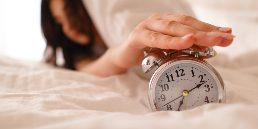 Women hitting alarm clock in bed